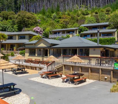 Outdoor seating area with picnic tables and umbrellas at a lodge surrounded by trees and plants.