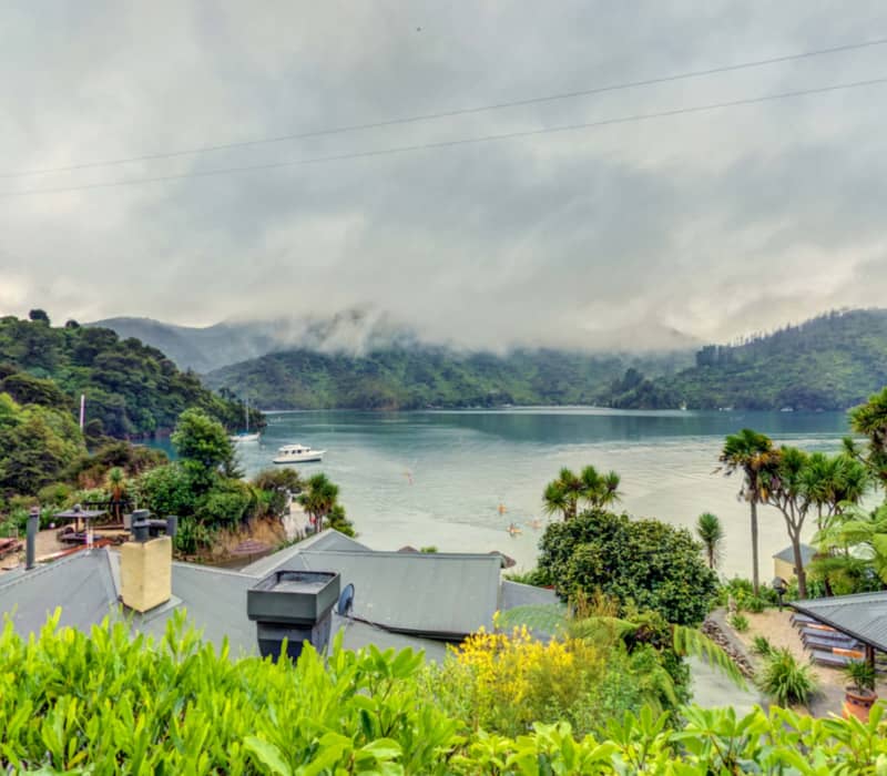 View of a tranquil bay with boats and green hills under cloudy sky from a lodge rooftop.