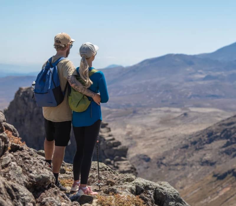 Couple standing on rocky terrain overlooking volcanic mountains during a hike.