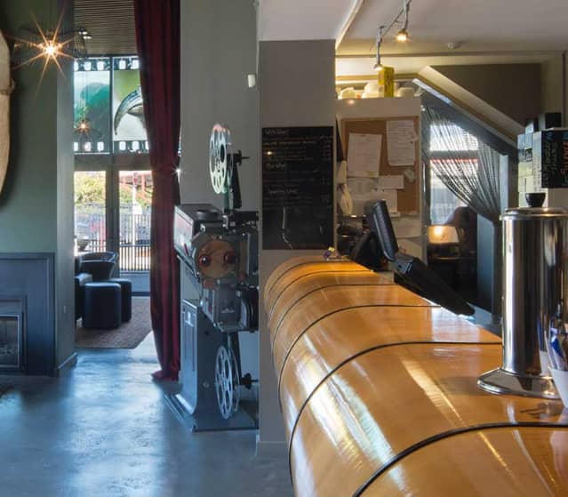 Cozy cinema bar interior with seating, movie projector, fireplace, and coffee counter.