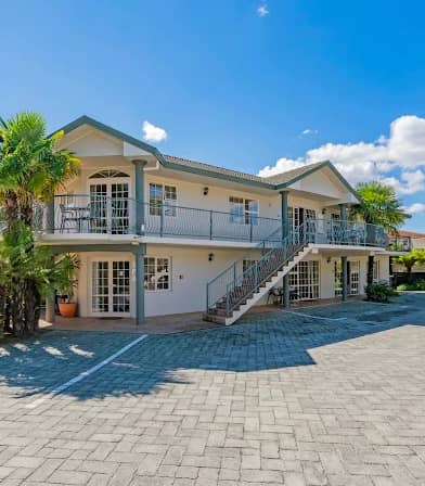 Elegant two-story spa building with balconies, stairs, palm trees, and clear blue sky