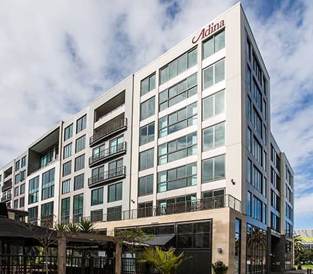 Modern multi-story hotel building with glass windows and balconies under a partly cloudy sky.