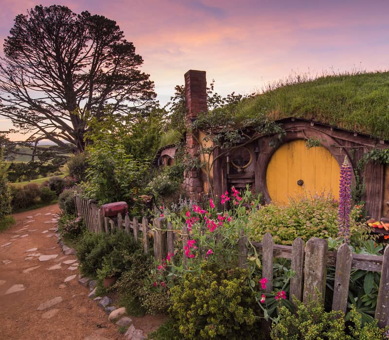Hobbit hole with a yellow door and garden at sunset on the Hobbiton movie set.