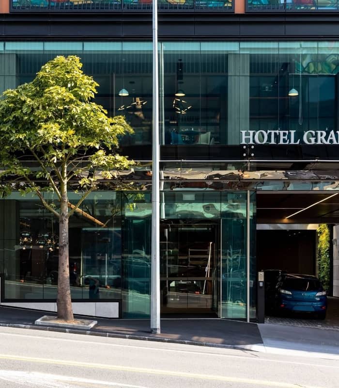 Modern hotel entrance with glass facade, tree, and car parked in driveway