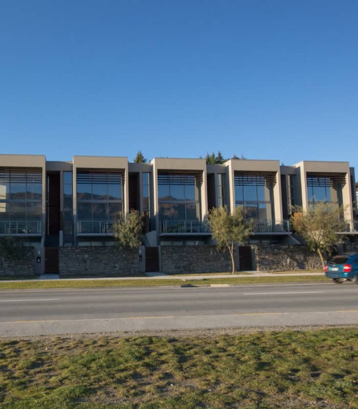 Modern residential buildings with large windows beside a road with a moving car under clear blue sky.