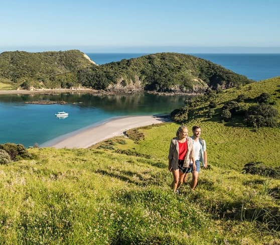 Couple hiking in Bay of Islands with scenic view of bay and boat.