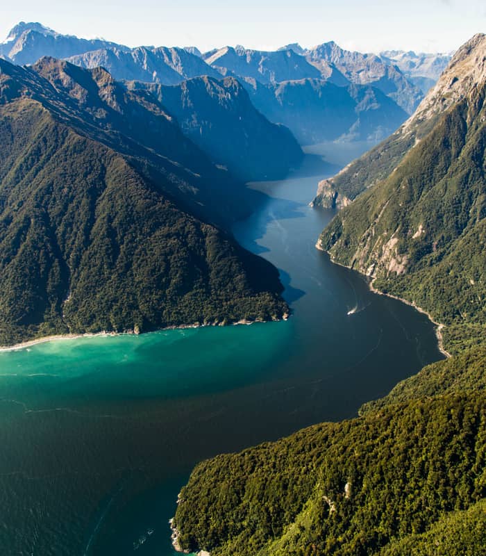 An aerial view of steep green hills with a deep blue water channel running down the middle 