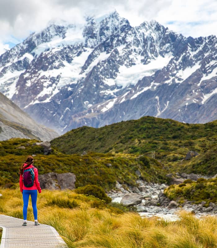 A person in bright colourful clothing standing on the walkway with Mt Cook in the background 