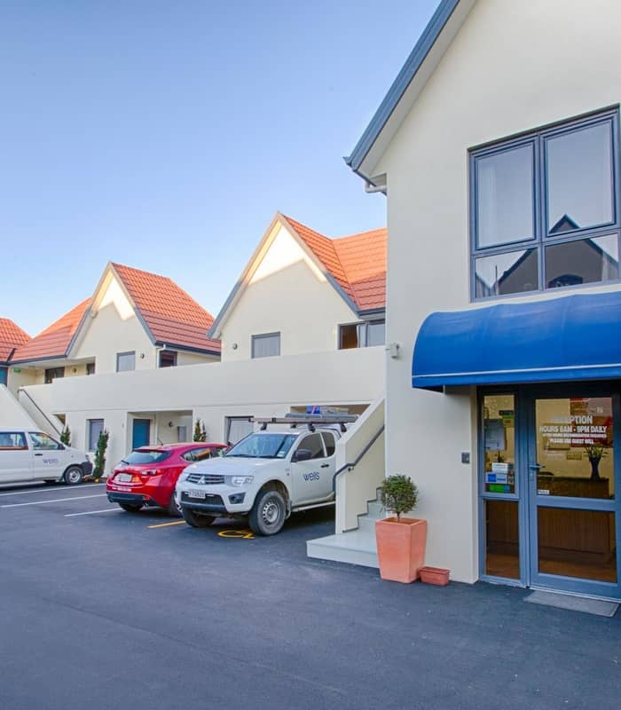 Motel building with blue awning reception entrance and cars parked alongside under clear blue sky.