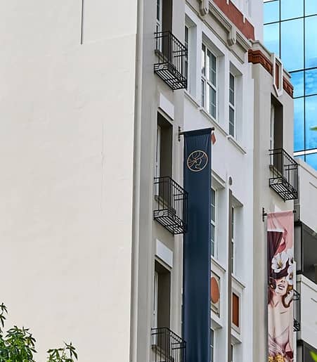 View of a modern building with banners, balconies, and surrounding trees under blue sky.