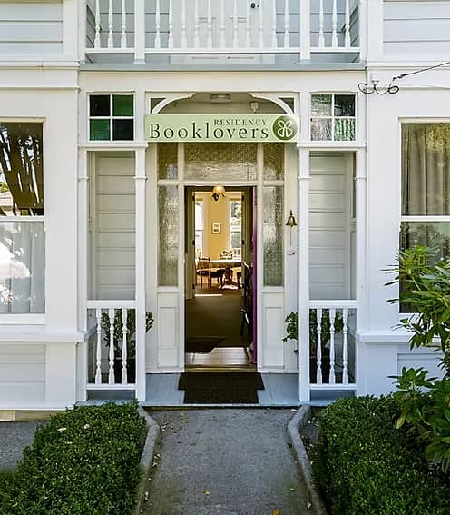 Entrance to Booklovers Residency B&B with white walls, windows, greenery, and a sign above the door.