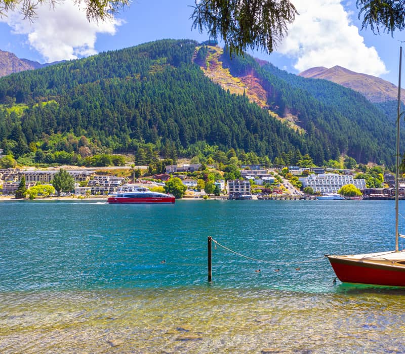 Looking out over Lake Wakatipu in Queenstown with a green hill and boats on the lake 