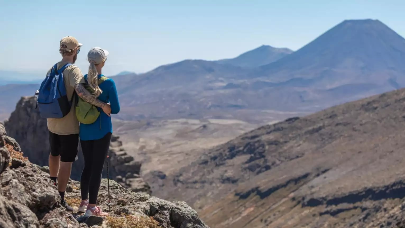 Couple standing on rocky terrain overlooking volcanic mountains during a hike.