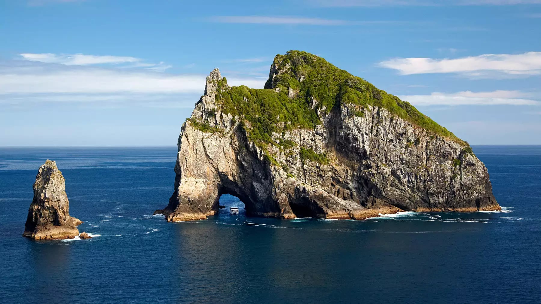 A large rock formation in the ocean with a natural tunnel archway, a popular tourist site in the Bay of Islands.