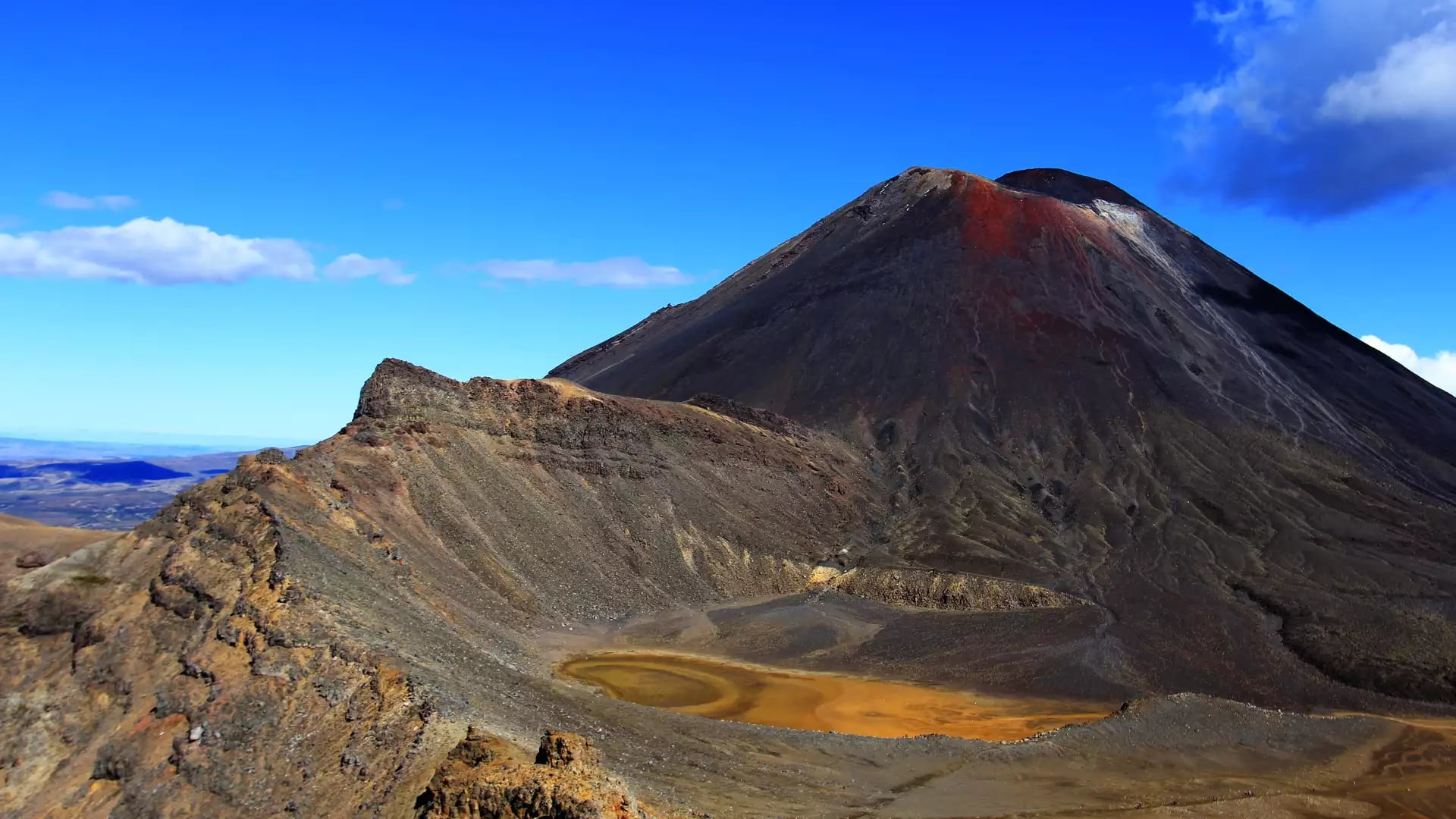 Mt Ngauruhoe volcano with orange crater lake under a clear blue sky